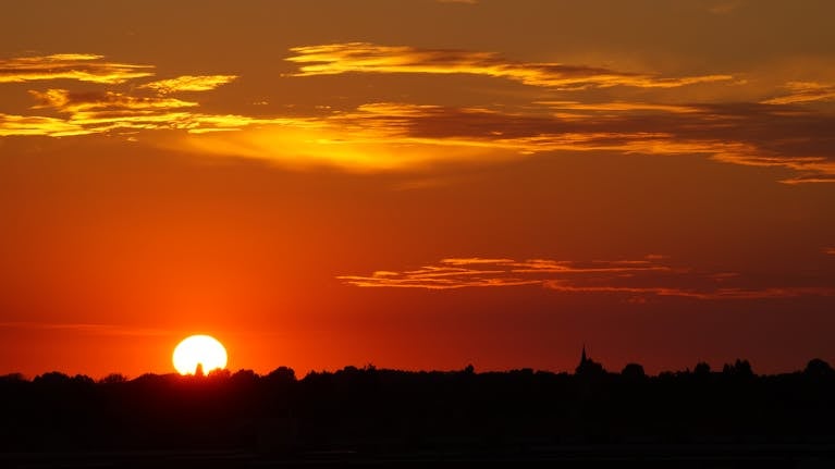 Vibrant sunset with silhouetted treeline creates a dramatic, warm sky.